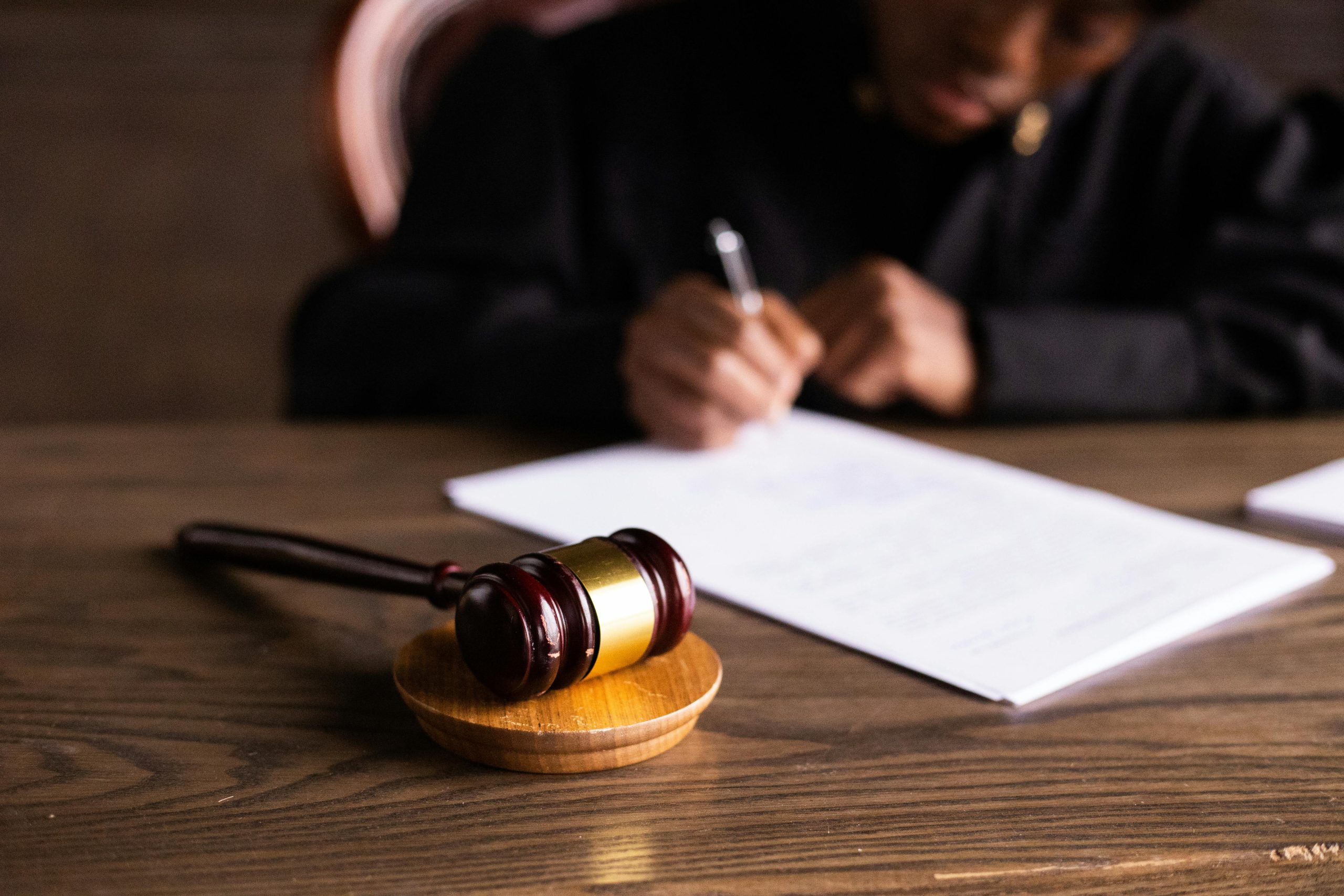 ICRA - A wooden gavel rests on a table in the foreground, while in the background, a person in a judge's robe diligently writes, possibly preparing an important ICRA report. The focus remains on the gavel, underscoring its significance within this legal context.