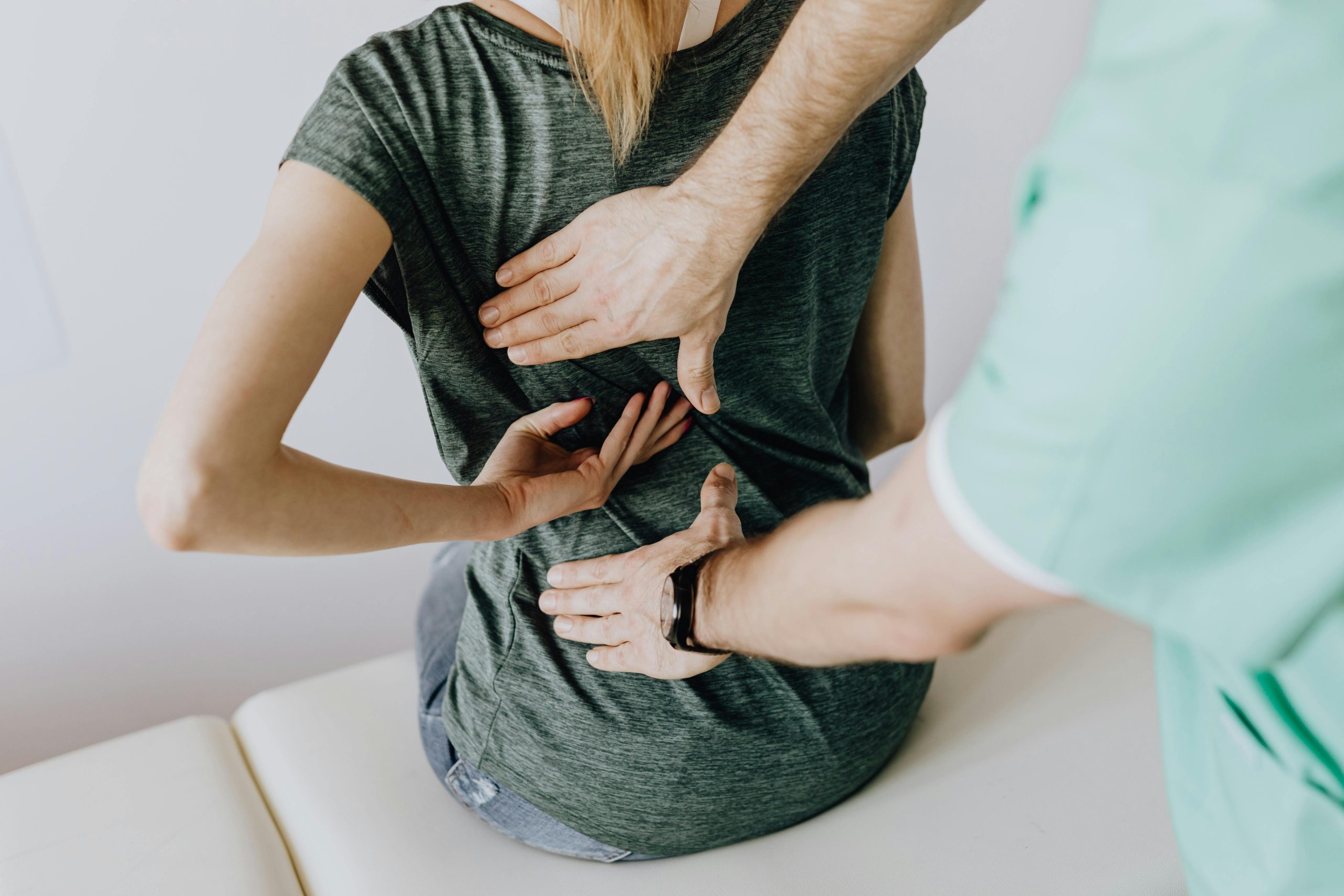 ICRA - A person sits on a medical examination table, undergoing an ICRA-compliant back assessment. The healthcare professional methodically places their hands on the individual's upper and lower back, attentively evaluating for any signs of pain or discomfort.
